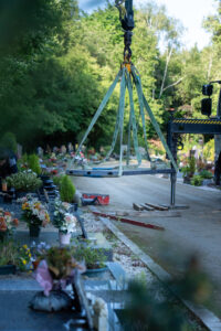 Grue soulevant pierre tombale dans un cimetière ensoleillé.
