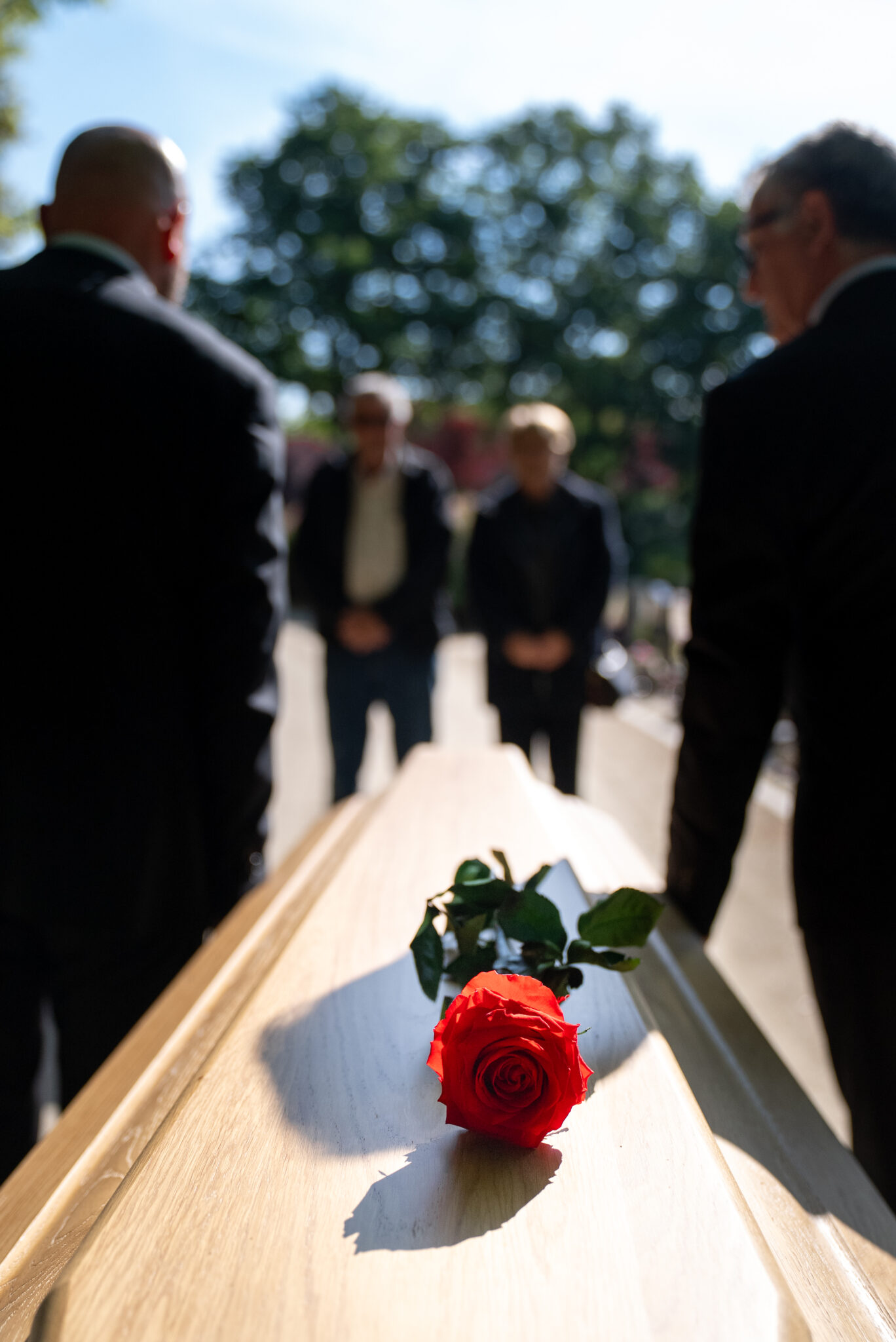 Cercueil avec rose rouge et personnes en arrière-plan.