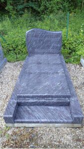 Tombe en marbre gris, fond végétation.